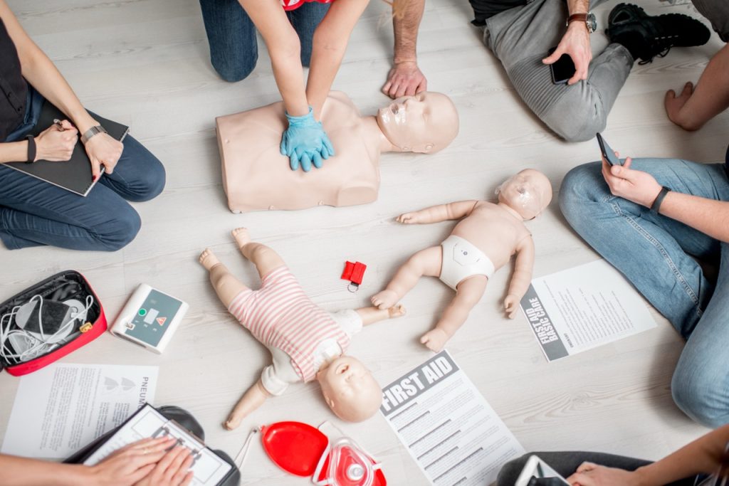 Group of people learning how to perform first aid and cpr heart compressions with dummies during the training indoors