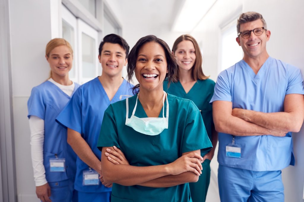 group of CNA students in blue and green colored scrubs standing in a medical facility hallway